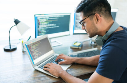 Side view of attractive Hispanic developer programming software using computer while working from home